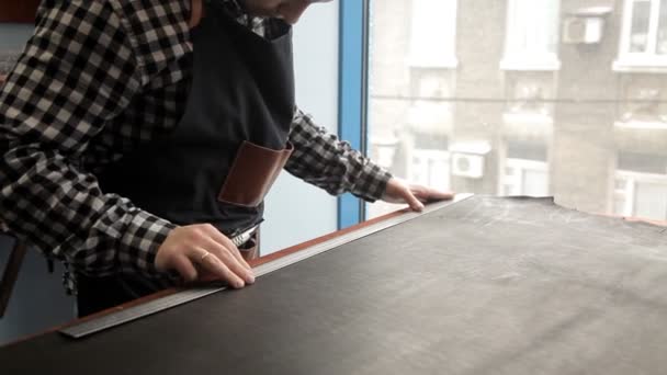 Um mestre de um leme de couro corta tarugos para fazer um cinto. Procedimento para o fabrico de cintos de couro . — Vídeo de Stock