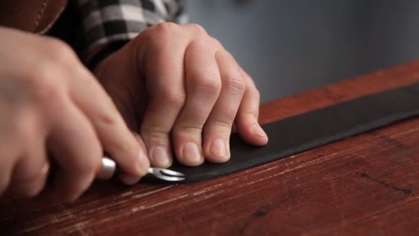 El especialista corta el exceso de piel en la pieza de trabajo debajo del cinturón con la herramienta adecuada. Procedimiento para la fabricación de cinturones de cuero — Vídeo de stock