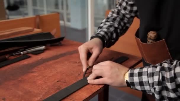 De specialist bezuinigingen overtollige huid op het werkstuk onder de riem met het juiste gereedschap. Procedure voor de vervaardiging van lederen riemen — Stockvideo