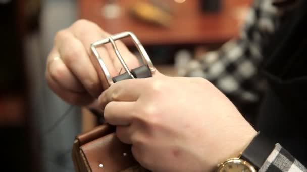 El maestro sujeta la hebilla en el cinturón de cuero, cose una aguja. Procedimiento para la fabricación de cinturones de cuero — Vídeos de Stock