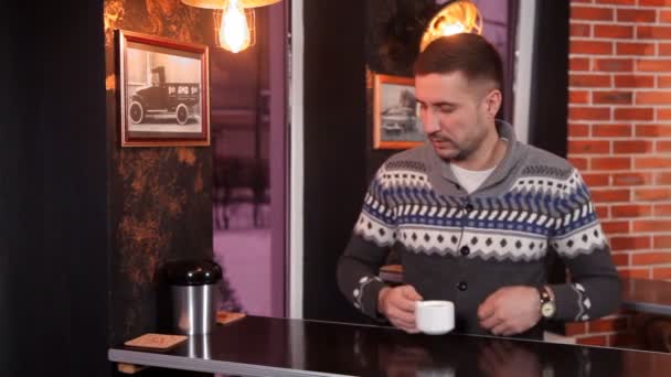 Carismático joven bebe café y utiliza un teléfono inteligente en un restaurante — Vídeos de Stock
