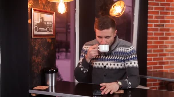 Carismático joven bebe café y utiliza un teléfono inteligente en un restaurante — Vídeos de Stock