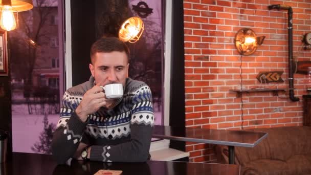 Karizmatik genç adam kahve içer ve bir restoranda bir akıllı telefon kullanır — Stok video
