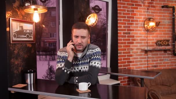 Carismático joven bebe café y se comunica por teléfono en un restaurante — Vídeos de Stock