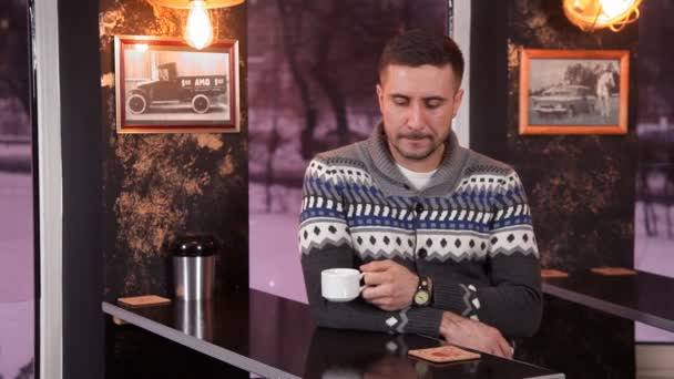 Χαρισματικός νεαρός πίνει καφέ και χρησιμοποιεί ένα smartphone σε ένα εστιατόριο — Αρχείο Βίντεο