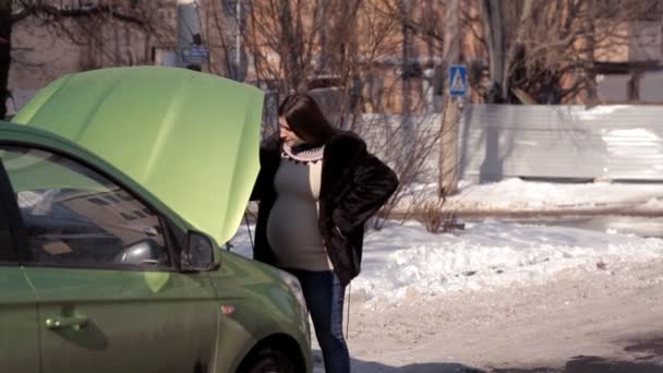 W zimie ciężarna dziewczyna szuka pomocy od przejeżdżających samochodów w naprawie uszkodzonego samochodu — Wideo stockowe