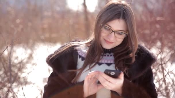 Jong meisje in een met sneeuw bedekte landing maakt gebruik van een mobiele telefoon, corrigeren van haar haren — Stockvideo