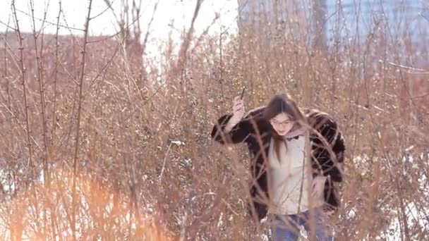 La chica camina en un aterrizaje cubierto de nieve en la ciudad de invierno y trata de coger una señal móvil en su teléfono — Vídeos de Stock