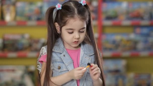 Непереборна маленька дівчинка грає з дитячим пластиковим конструктором та іншими предметами в дитячій кімнаті — стокове відео