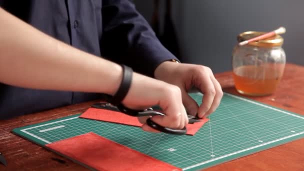 В мастерской мужчина приклеивает заготовки кожи, делая бумажник — стоковое видео