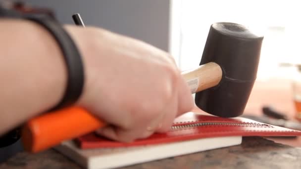 The man punches the holes in the leather blank with a hammer and a special tool — Stock Video