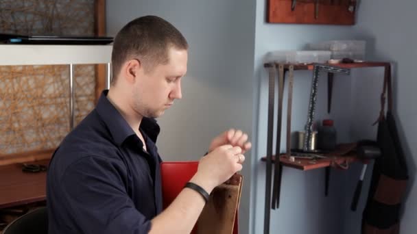 In the workshop, a man is sewing leather workpieces, making a wallet — Stock Video