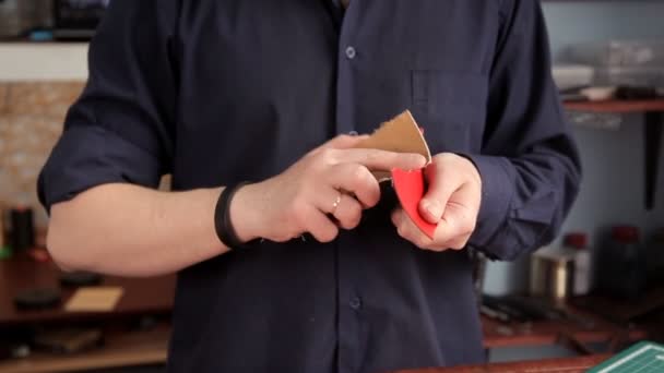 Man met schuurpapier verwijdert onregelmatigheden op een product van leer — Stockvideo