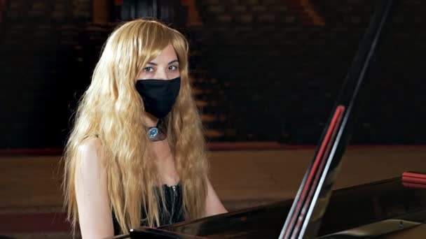 Siyah elbiseli ve yüzünde maske olan bir kız piyano çalıyor. Alışılmadık müzik performansı — Stok video