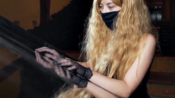 En blondin i svart klänning och mask smeker försiktigt pianot. Ovanligt blond visar känslor för pianot — Stockvideo