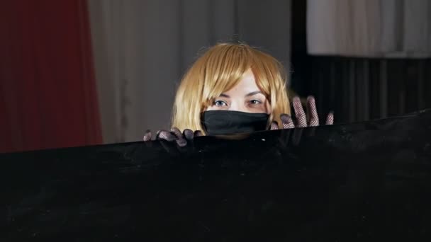 Niezwykła blondynka w masce z wielobarwnymi oczami zabawnie dotyka i chowa się za Pionino — Wideo stockowe