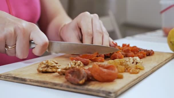 Молодая домохозяйка режет сухофрукты - сушеные абрикосы с ножом на доске. Концепция здорового питания — стоковое видео