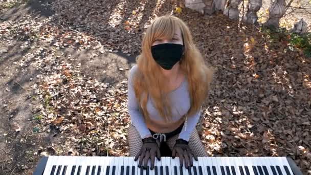 Eine junge sexy Frau spielt im Herbst auf der Straße Synthesizer, mit nacktem Bauch und schwarzer Maske im Gesicht. Musikstil, Grunge-Instrument. Pop und klassische Musik, Melodie — Stockvideo