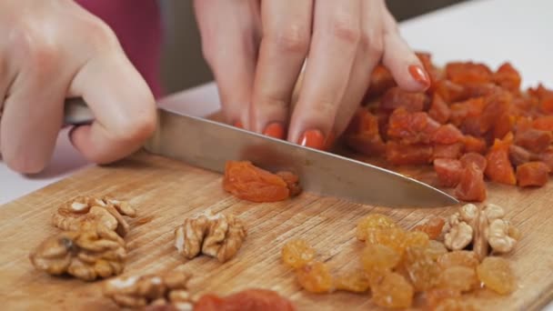 Een jonge huisvrouw snijdt gedroogd fruit - gedroogde abrikozen met een mes op een snijplank. Gezond eten concept. Langzame beweging — Stockvideo
