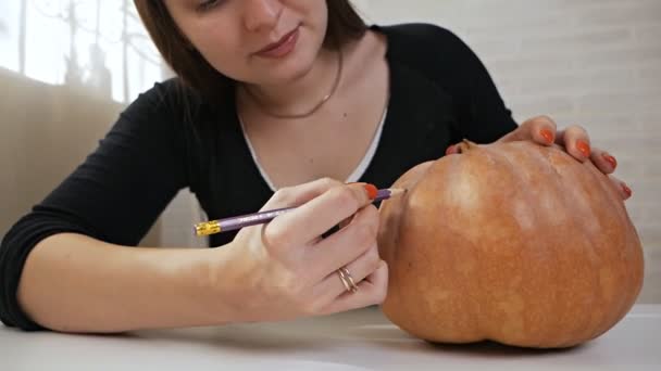 Concetto di Halloween, ragazza felice seduta a un tavolo con zucche, occhi e bocca dipinti su una zucca di Halloween — Video Stock