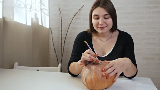 Concetto di Halloween, ragazza felice seduta a un tavolo con zucche, occhi e bocca dipinti su una zucca di Halloween — Video Stock