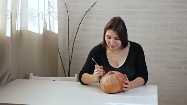 Concetto di Halloween, ragazza felice seduta a un tavolo con zucche, occhi e bocca dipinti su una zucca di Halloween — Video Stock