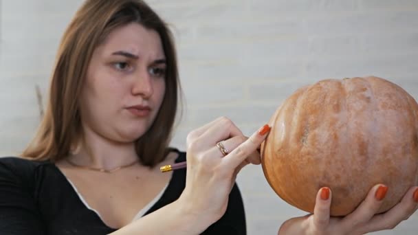 Concetto di Halloween, ragazza felice seduta a un tavolo con zucche, occhi e bocca dipinti su una zucca di Halloween — Video Stock