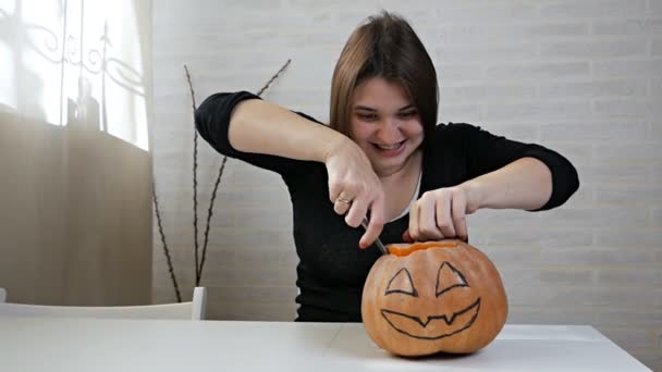 Vrouw met een gekke blik en blik, het bereiden van een pompoen op een Halloween feest op de keukentafel, een meisje snijdt haar mond uit met een mes — Stockvideo