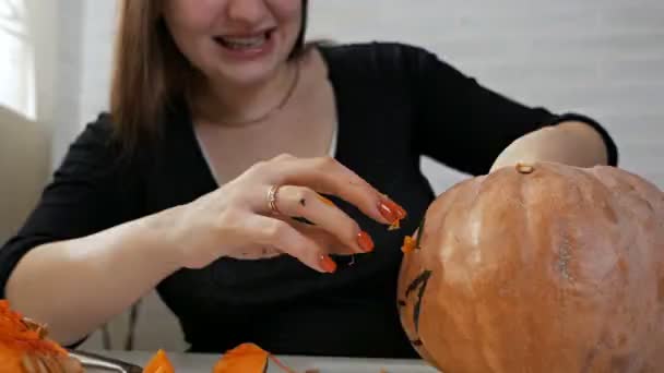 Orange pumpkin carved for the celebration of Halloween. A woman with a crazy look takes out seeds and pulp from a pumpkin. Preparing the scenery for a traditional fall party. Crazy halloween — Stock Video