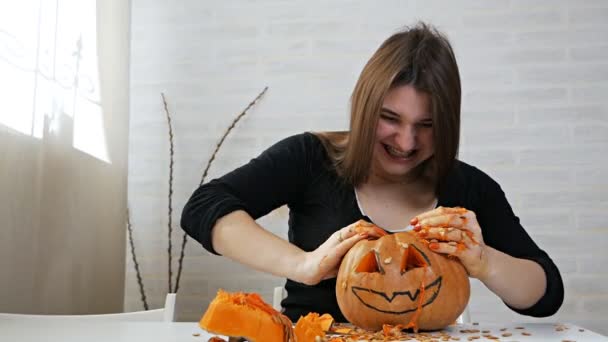 ハロウィンのお祝いのために刻まれたオレンジカボチャ。狂気の表情をした女性は、カボチャから種とパルプを取り出します。伝統的な秋のパーティーのための風景を準備します。クレイジーハロウィン — ストック動画