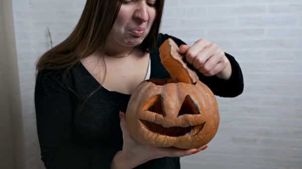 Een jong meisje houdt een vermiste pompoen in haar handen na het vieren van Halloween. Ontbrekende pompoen en slechte geur, walging op het gezicht — Stockvideo