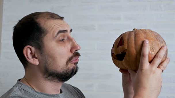 Ein Mann hält einen geschmorten Kürbis in den Händen, nachdem er Halloween gefeiert hat und improvisiert mit einem Kürbis kommuniziert — Stockvideo