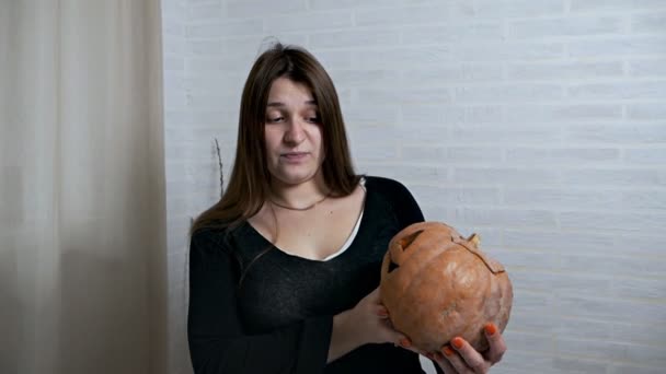 Una joven sostiene una calabaza perdida en sus manos después de celebrar Halloween. Falta calabaza y mal olor, disgusto en la cara — Vídeo de stock