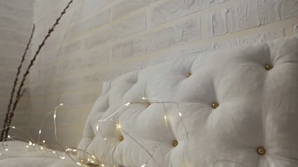 Un canapé blanc avec coussins est décoré avec des lumières de vacances.Décorations de Noël pour la célébration — Video