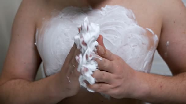 Un joven sin camisa que se pone espuma de afeitar en la palma de la mano mientras se prepara para afeitarse el pecho. depilación mamaria en hombres — Vídeo de stock