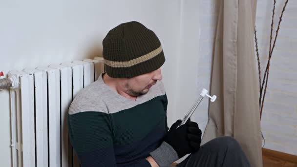 Mannen kontrollerar temperaturen på uppvärmningsbatteriet. Kall vinter, kallt i huset, lägenhet. En man värmer sig nära ett uppvärmningsbatteri — Stockvideo
