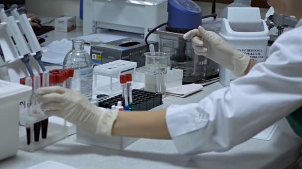 Mujer científica que mira una muestra de sangre en un tubo de ensayo en un laboratorio. Análisis de sangre de laboratorio — Vídeos de Stock