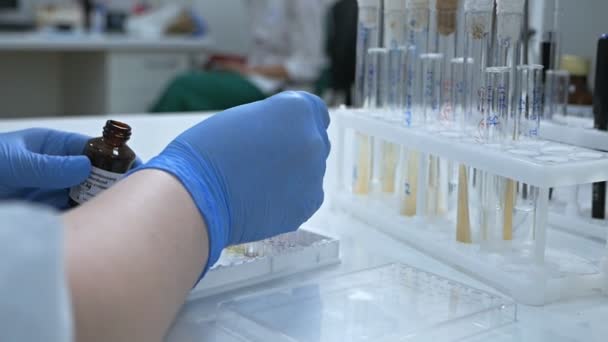 特定の疾患への獲得免疫の活性化を提供する生物学的薬剤の作成.大規模な近代的な研究室でマイクロピペットを埋めるために試験管を使用して女性研究者. — ストック動画