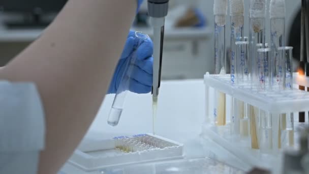 A criação de uma droga biológica que proporciona a ativação da imunidade adquirida a uma doença específica. Pesquisadora usando tubos de ensaio para preencher uma micropipeta em um grande laboratório moderno . — Vídeo de Stock