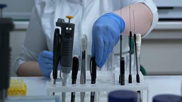 Μια γυναίκα χημικός σε ένα τραπέζι σε ένα εργαστήριο διεξάγει ένα επιστημονικό πείραμα με χημικές ουσίες. Ερευνητής που στάζει χημικές ουσίες σε δοκιμαστικούς σωλήνες σε εργαστήριο. — Αρχείο Βίντεο