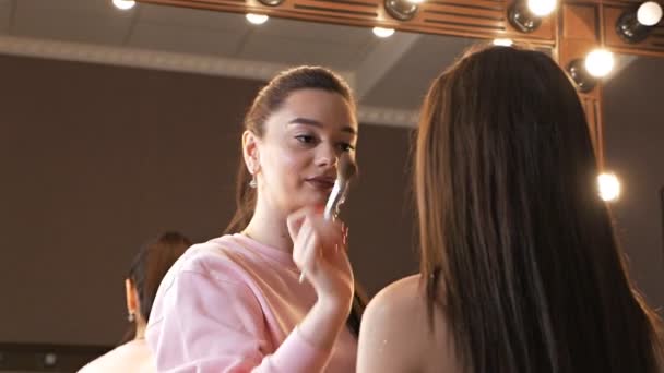 Maquillaje artista aplicar polvo facial a una hermosa joven, una actriz famosa con el pelo largo para disparar en un clip. Maquillaje facial — Vídeos de Stock