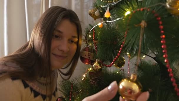 Mooi meisje in een trui versiert de kerstboom met ballen. Prachtig kerstinterieur — Stockvideo