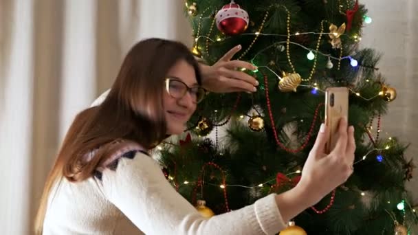 スマートフォンでクリスマスの自撮りをする陽気な若い女性。ホリデー、新年、幸福の概念 — ストック動画