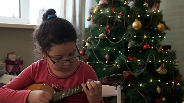 Девушка играет в домбру на фоне украшенной елки — стоковое видео