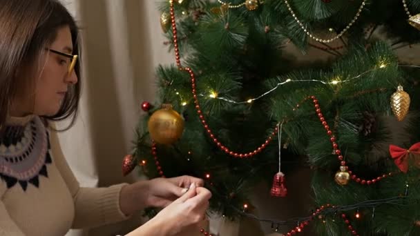 Attractive young blonde woman decorating christmas tree with baubles — Stock Video