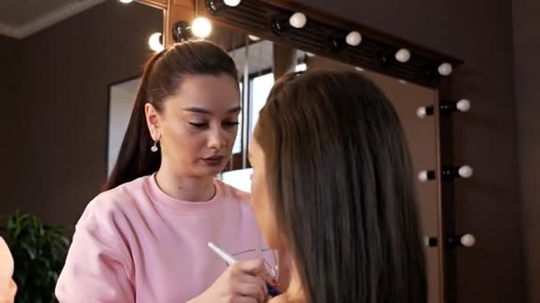 Maquiagem artista faz maquiagem corporal usando pó. Menina bonita nova com cabelo longo faz maquiagem em um salão de beleza — Vídeo de Stock