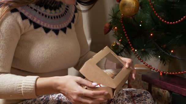 Mladá dívka narovnává stuhu na dárku, který drží. Žena balí vánoční dárky — Stock video