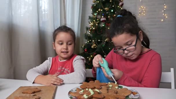 Crianças pequenas decoram biscoitos de gengibre de Natal com creme em um fundo da árvore de Natal.Biscoitos de Natal em casa — Vídeo de Stock
