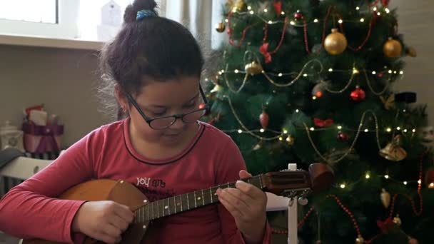 Meisje speelt dombra tegen de achtergrond van een versierde, kerstboom — Stockvideo