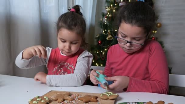 小さな子供たちはクリスマスツリーの背景にクリームとクリスマスジンジャーブレッドクッキーを飾る。 — ストック動画